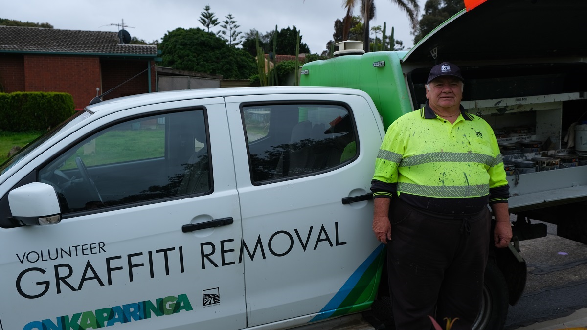 Neville Radford stands alongside a colourful City of Onkaparinga graffiti removal ute in his high-vis paint-splashed shirt and cap.
