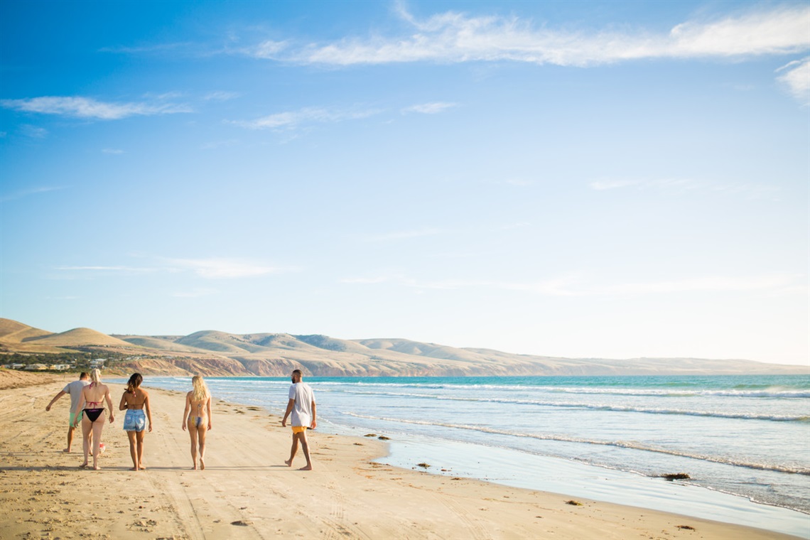 A group of people walk along Silver Sands beach on a sunny blue-sky day.