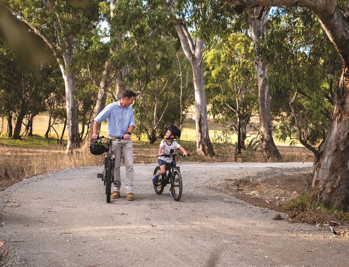 Boy riding bike with Father watching on