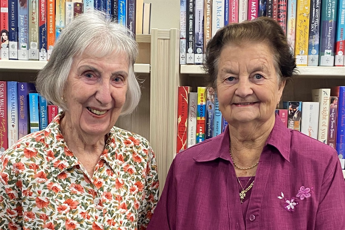 Hetty Browning and Phyllis Corin smiling in front of a library bookshelf.