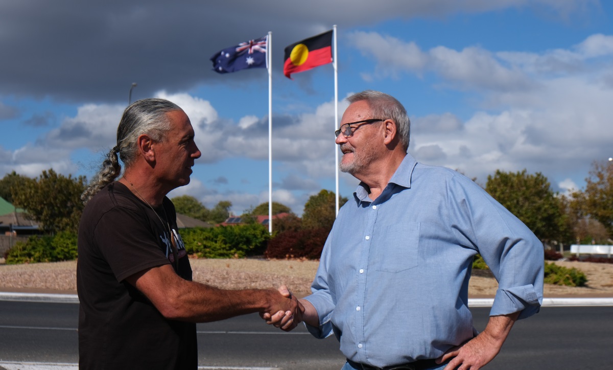 Karl Telfer with Councillor Richard Peat at the Seaford roundabout in front of the Aboriginal flag.