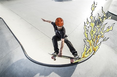 A skateboarder grinds along the coping of a ramp, with illustrated flames coming off his wheels and trucks.