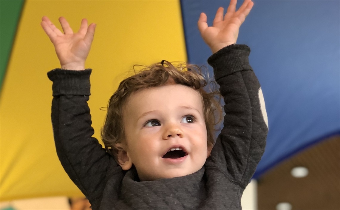 A young boy smiles with his hands in the air at a children's storytime session.