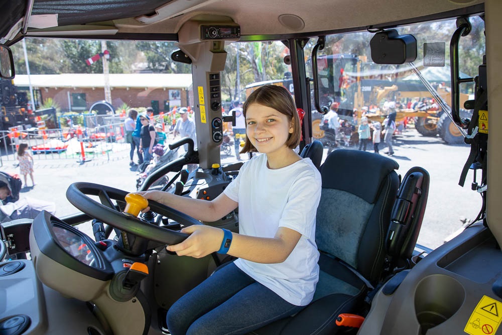 A smiling girl sits inside the cab of a truck holding the steering wheel.