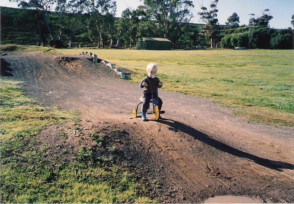 Sam Willoughby as a toddler riding a trike on a track with a dummy in his mouth.