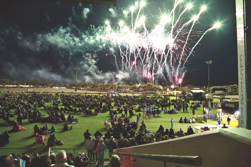 Fireworks illuminate the sky above the South Adelaide Football Club oval over the heads of a large night-time crowd.