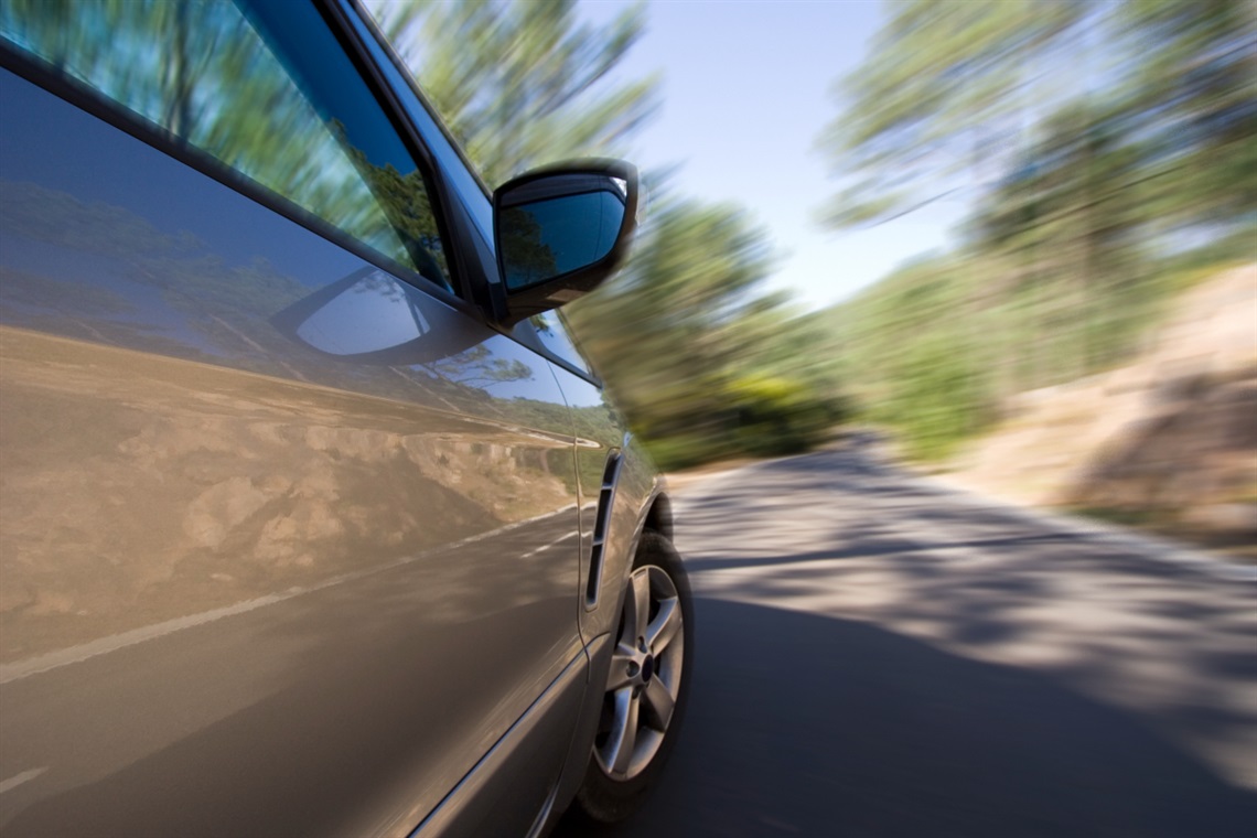 The view from a car as it drives along a country road, with the road and trees blurred due to speed.