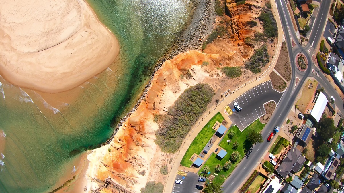 An aerial view of the coast, including red cliffs, carparks, roads and the Onkaparinga rivermouth near South Port beach.
