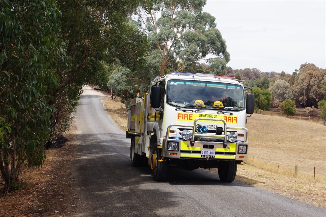 A white Seaford CFS fire truck drives towards the camera on a tree-lined rural road.