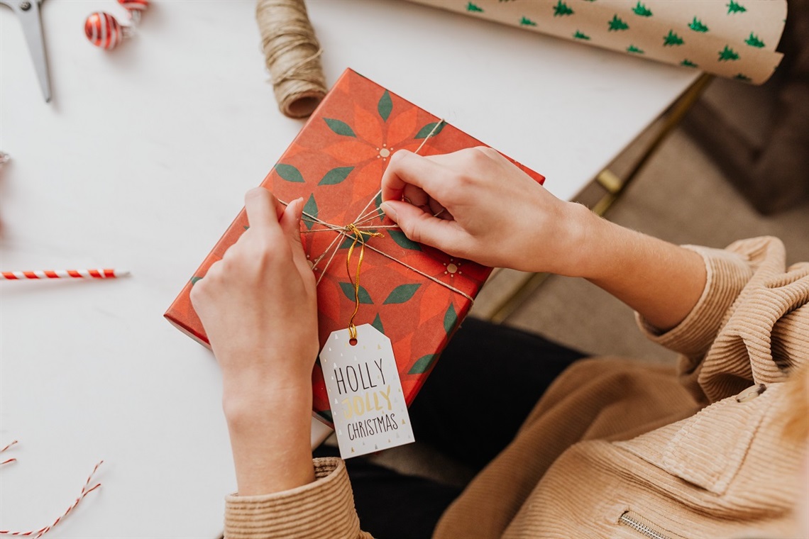 A person ties string around a red-wrapped christmas gift with a label that reads 