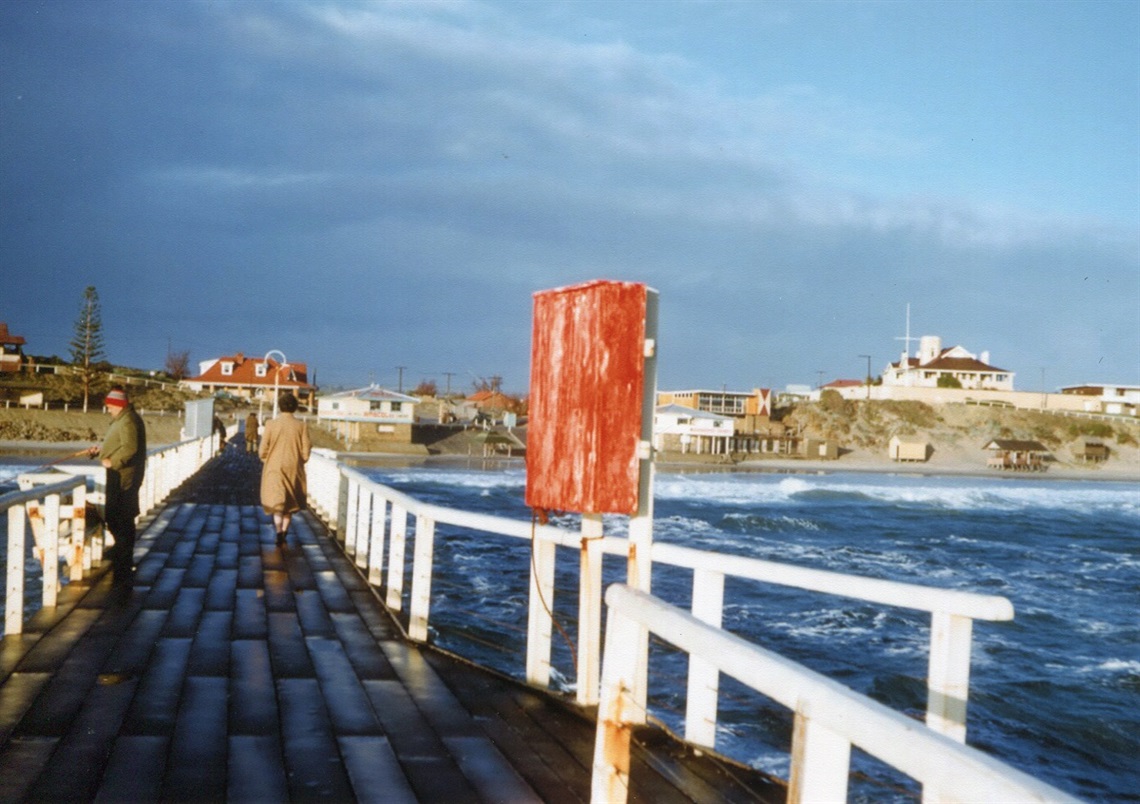 A view from the Port Noarlunga jetty towards the sand dunes with a fisherman and walkers in the 1960s.