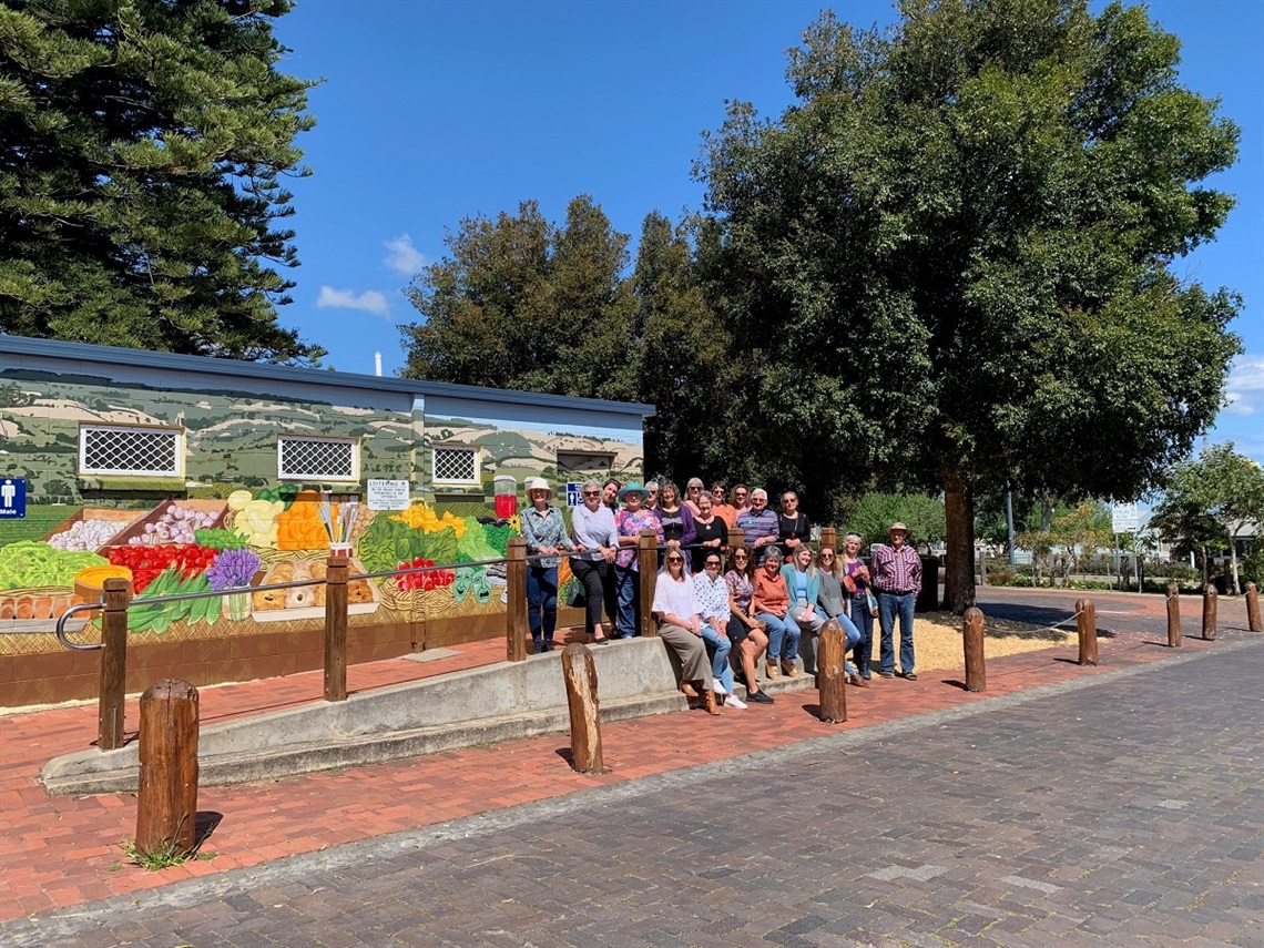 A large group of volunteers stand in front of a colourful mural on a toilet block in Willunga Town Square.