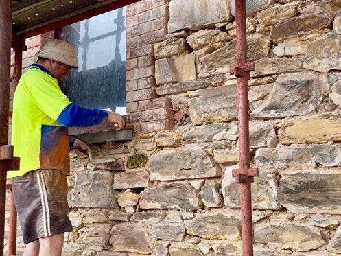 A skilled tradesperson in a high-vis shirt works on the stone wall exterior at 35 High Street, Willunga.