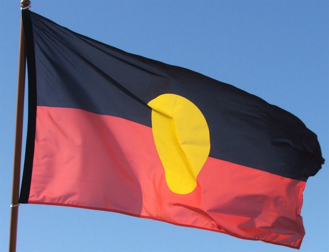 A photo of the Aboriginal flag flying amid a blue sky.