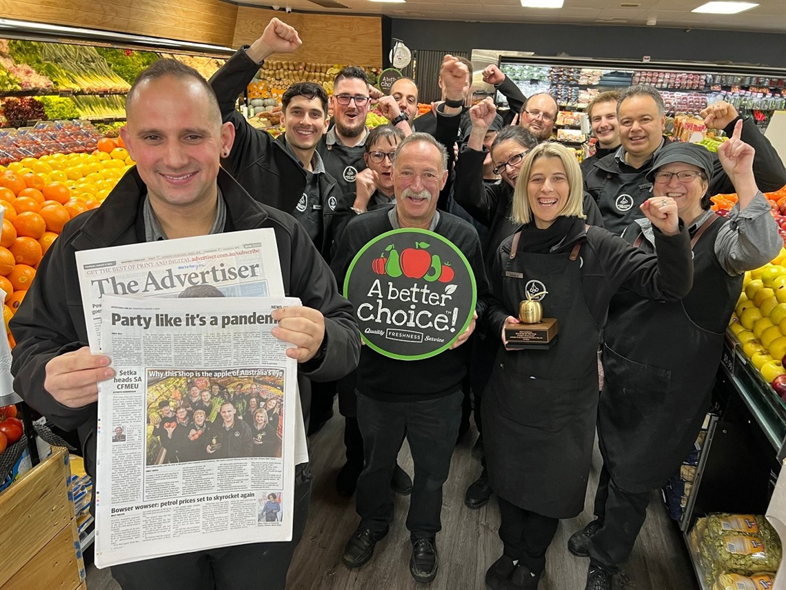 The smiling team at Adelaide Fresh Fruiterers pose with their awards and newspaper clippings about their win in the middle of their colourful fresh produce-lined store.