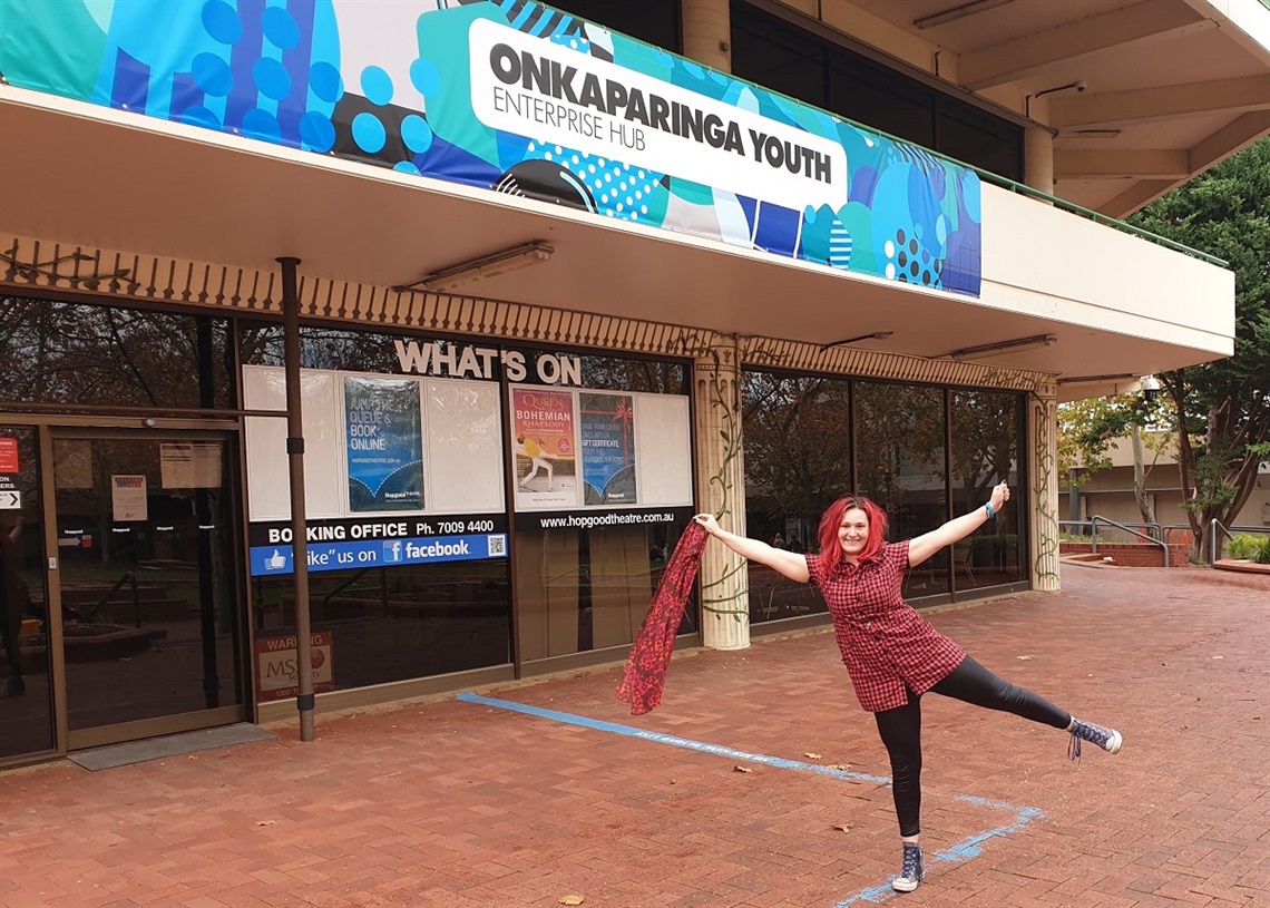 Onkaparinga Youth volunteer Blaze Pilgrim smiling with her arms outstretched in a red dress in front of the Onkaparinga Youth Enterprise Hub.