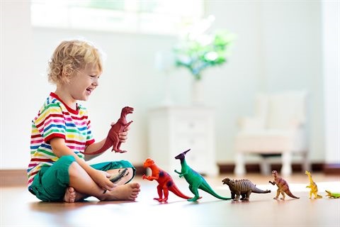A smiling boy sits on the floor alongside a row of dinosaur toys.