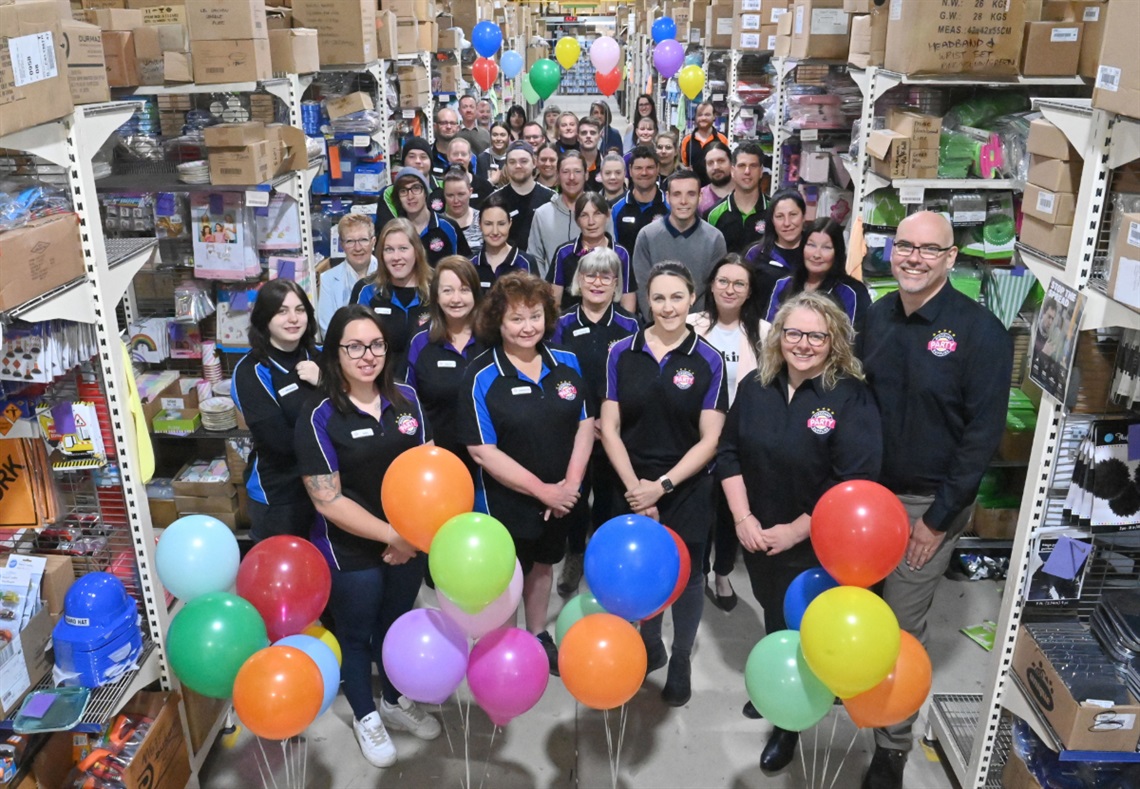 The growing team at Discount Party Supplies huddles around boxes and balloons.