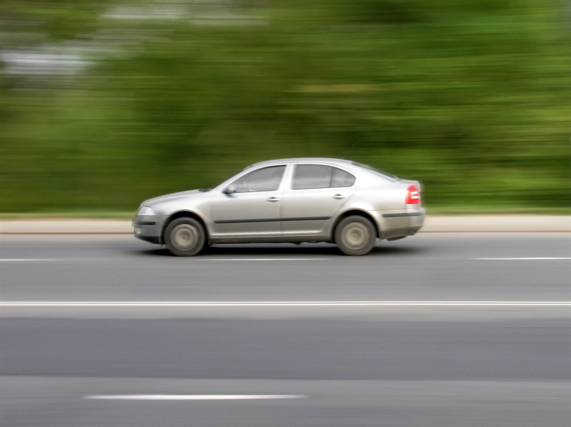 A blurred grey car moves quickly along a highway.