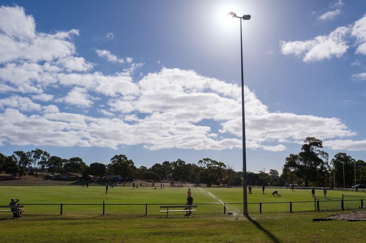 A view of the oval with football players training under a blue sky with white clouds.