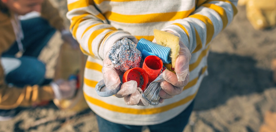 A person with gloved hands holds a handful of colourful litter picked up from a beach.