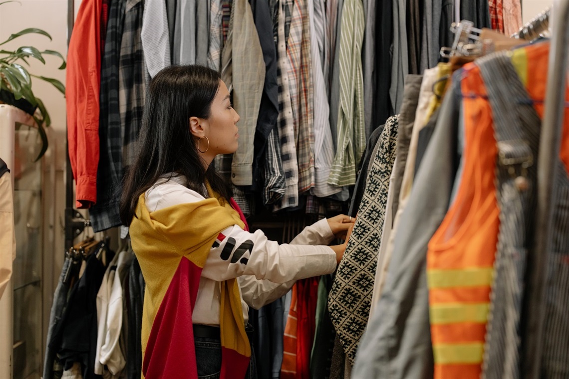 An Asian woman looks through a rack of clothing at an op shop.
