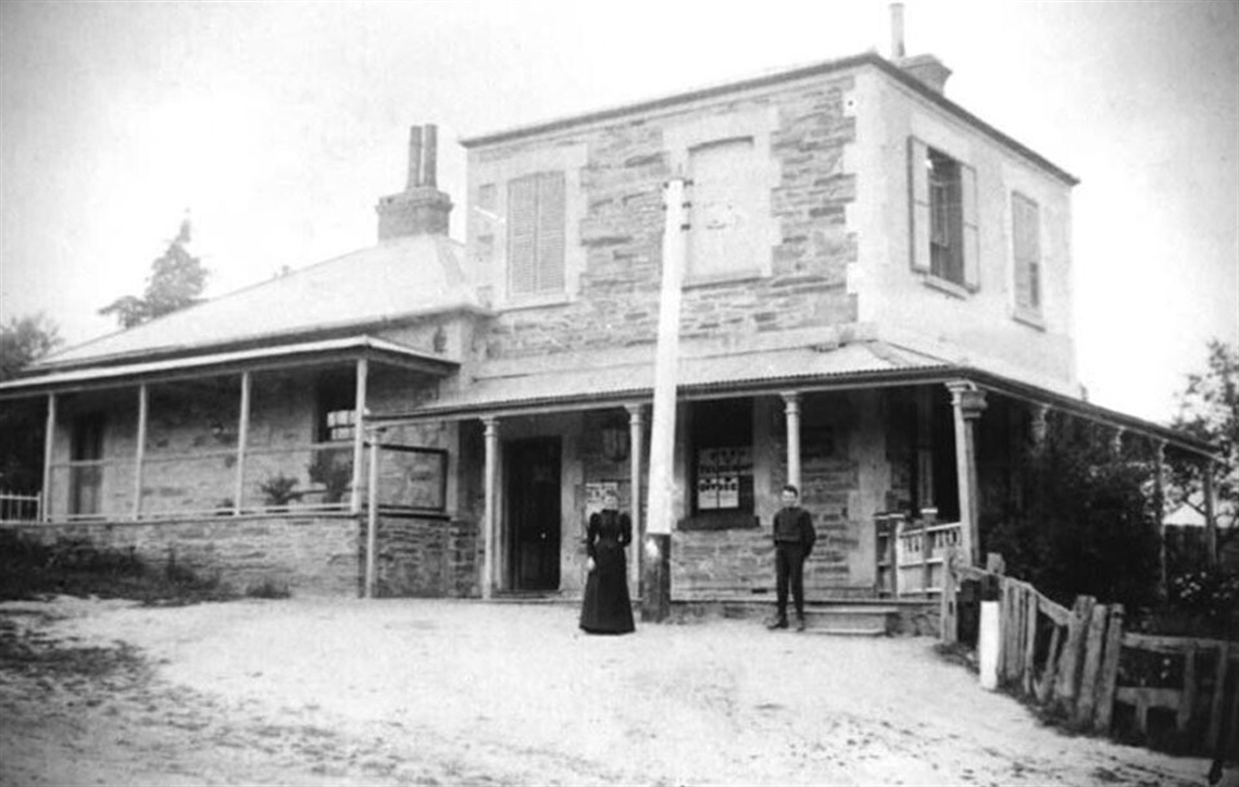 A black-and-white image of a man and a woman standing in front of the Willunga Post and Telegraph Office circa 1880.