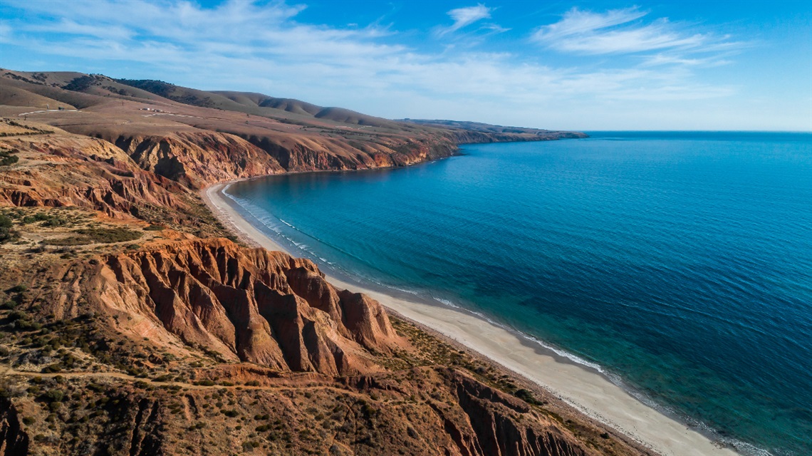 A view of the golden cliffs of Sellicks Beach alongside the still azure ocean.