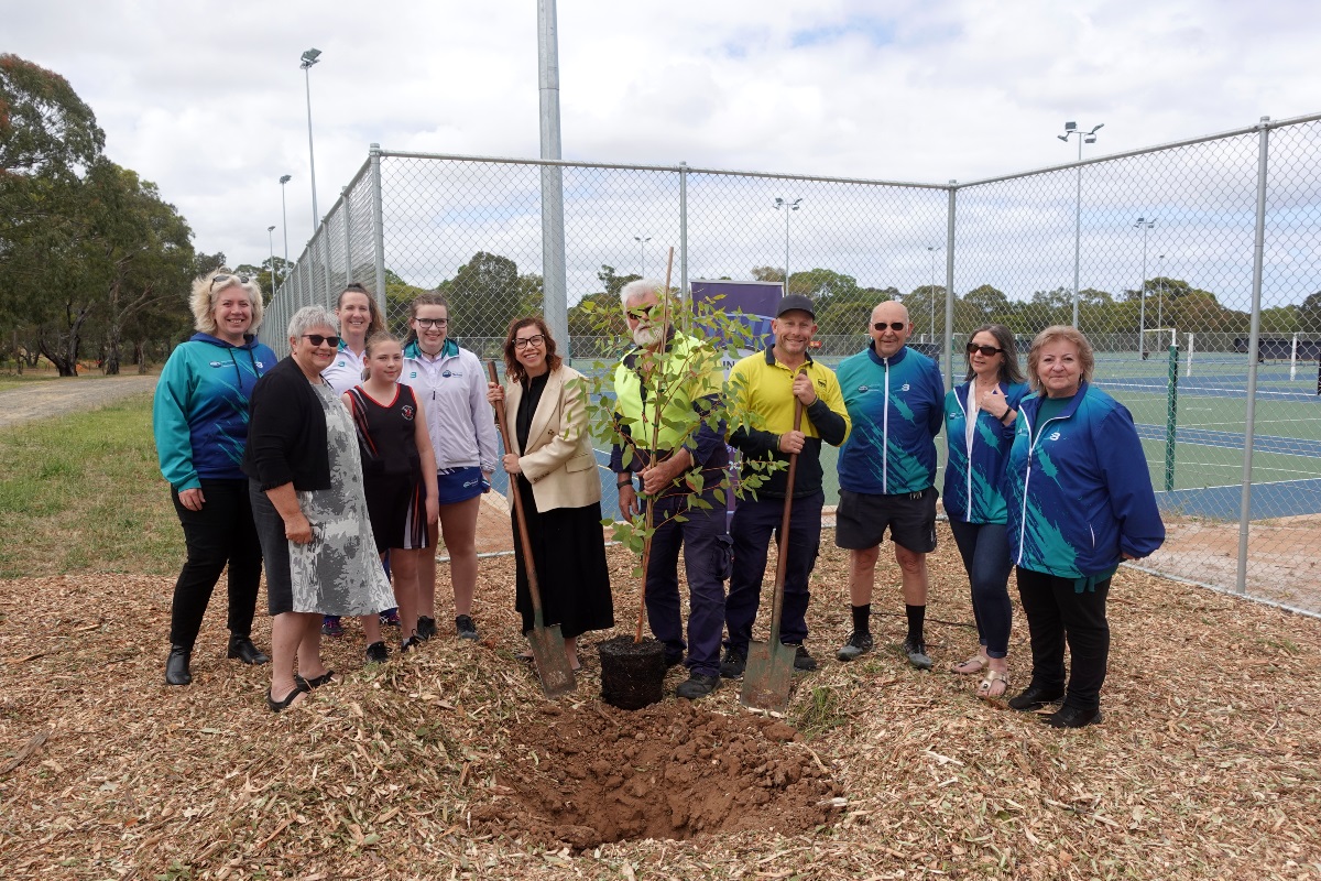 Amanda Rishworth MP and Mayor Moira Were smile with the new tree at Southern United Netball Association at Morphett Vale alongside council staff and netball club members.