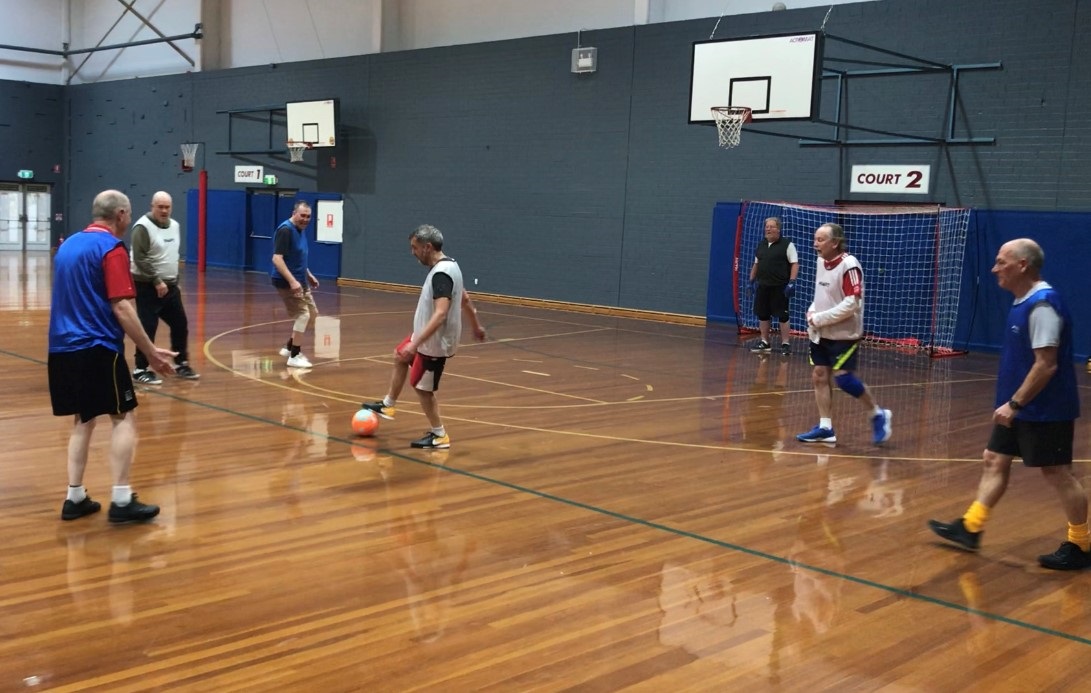 Players at the Noarlunga walking football group kick the ball to one another on the hard courts of Noarlunga Recreation Centre.