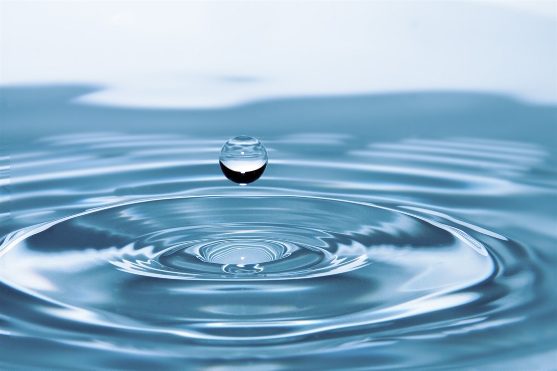 A close-up of a falling water droplet and the rippled surface of water beneath.