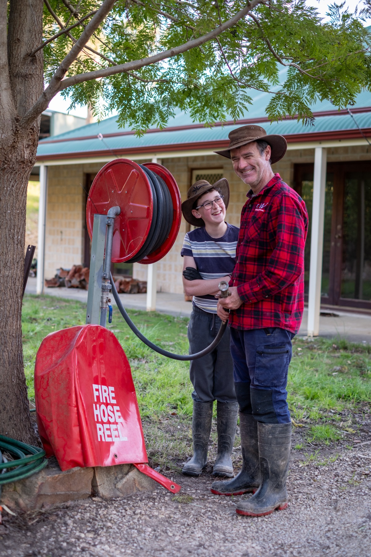 Andrew Ayles and his son laugh alongside a fire hose reel on their property.