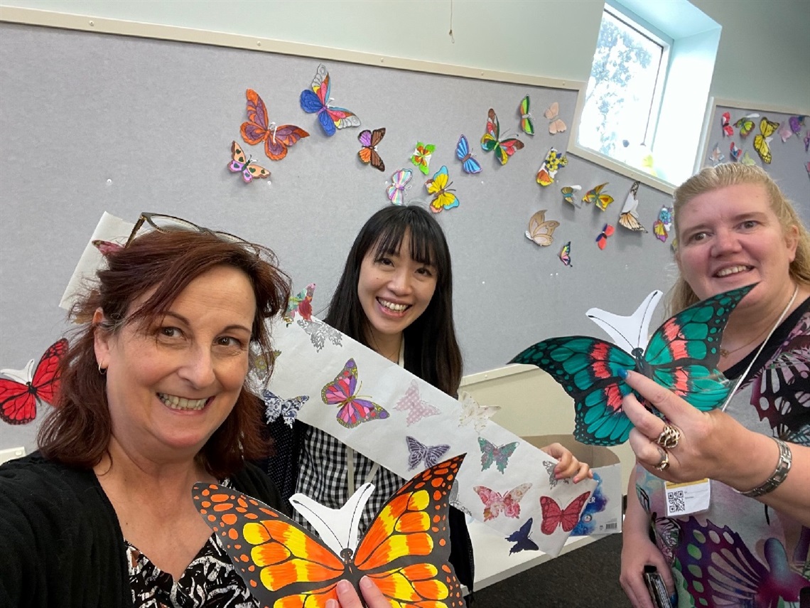 Three women with illustrated butterflies as part of a display at Hackham West Community Centre in 2021.