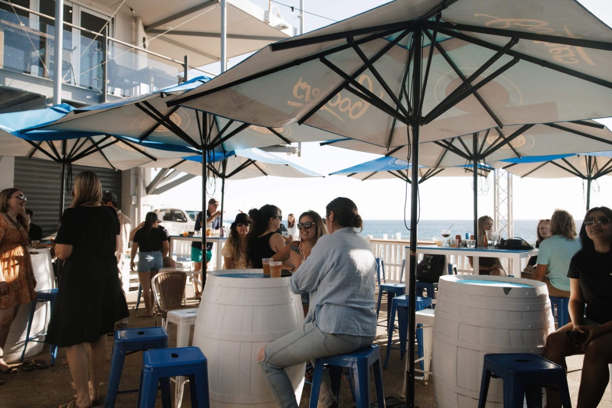 Diners drink beer at wine barrel tables under umbrellas.