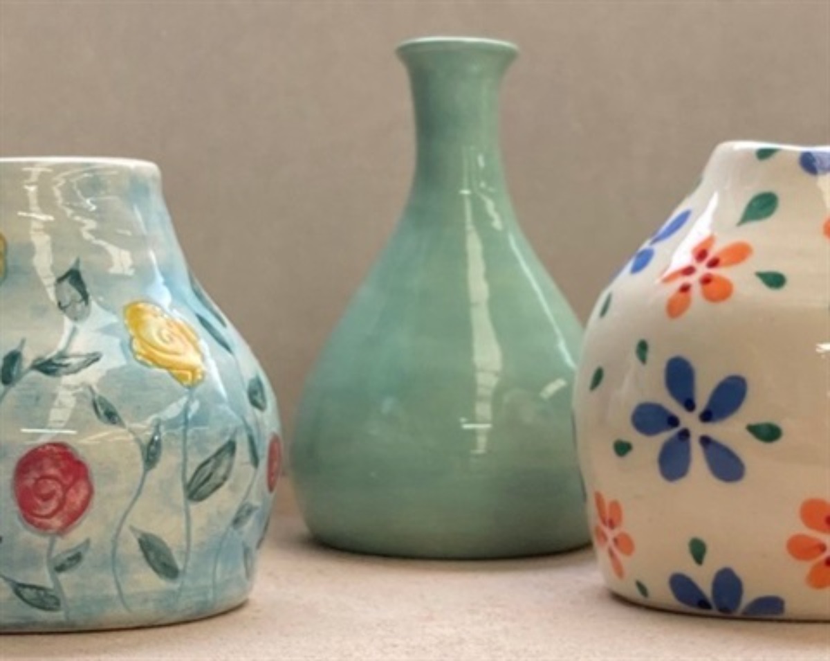A photograph of three painted ceramic vases, two featuring flowers, and a blue-green one in the middle.