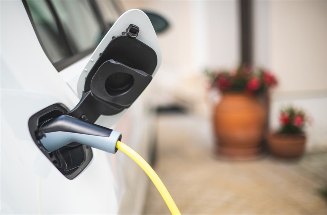 A photo of an electric vehicle charger plugged into a white car with two terracotta-potted plants in the background.