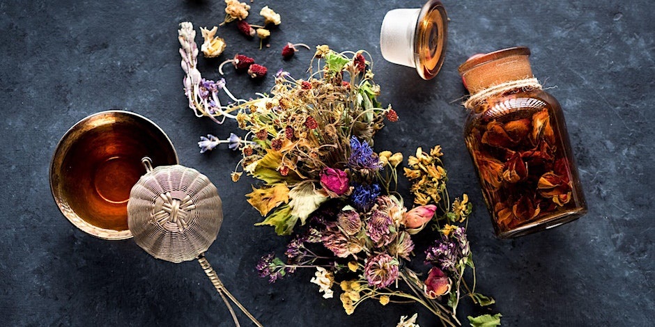 Herbs and a bowl and jar of herbal tea on a charcoal grey tabletop.