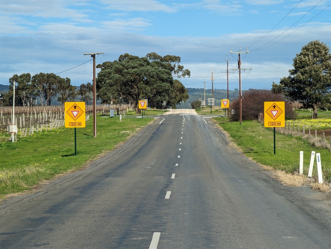 A series of bright yellow give way signs ahead of an intersection on a sunny day in McLaren Vale.