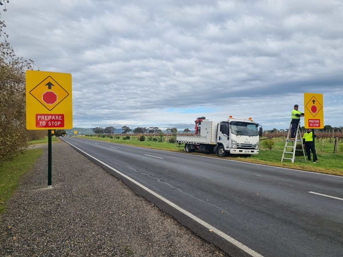 Council workers help to erect new stop signs on the side of a McLaren Vale road.