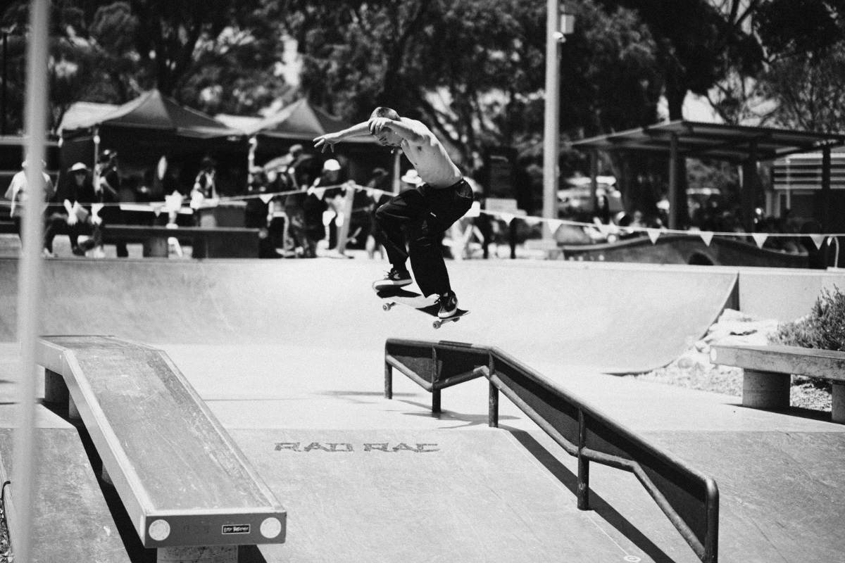 A black-and-white photo of a shirtless skateboarder grinding along a rail.