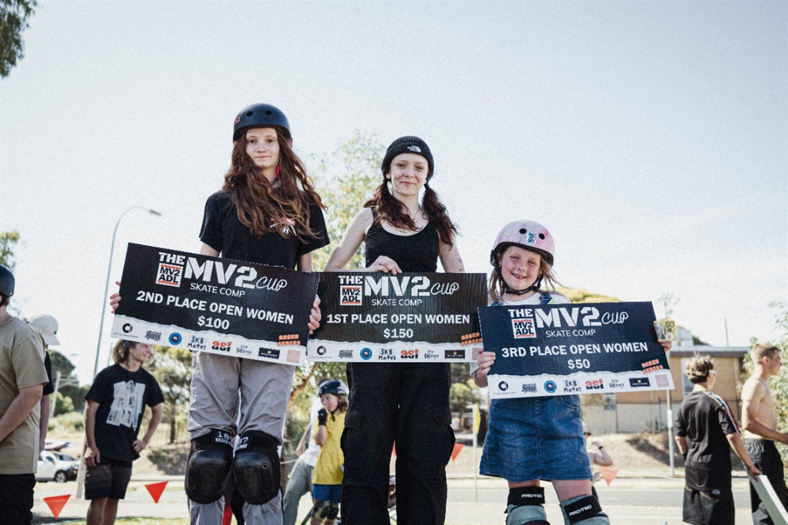 Three young women in skateboarding gear smile with their Mv2 Adl Cup awards.