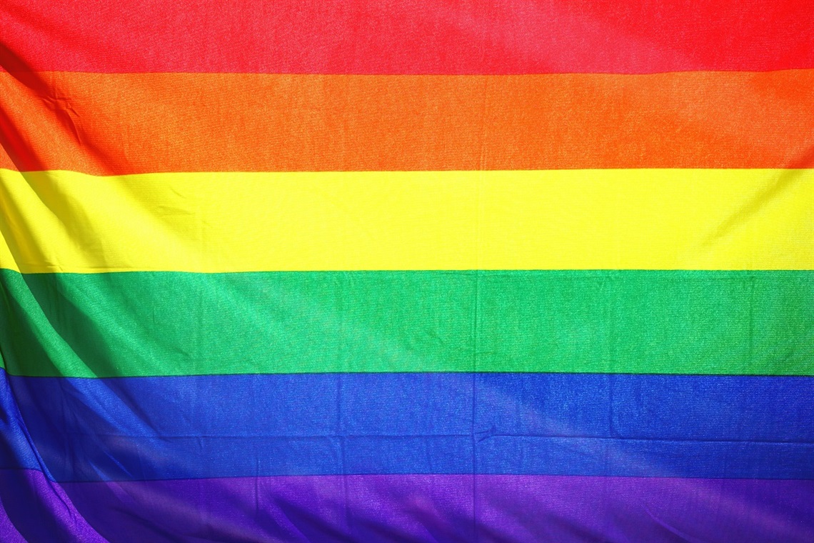 A close-up image of a Pride flag, with the colours of red, orange, yellow, green, blue and purple stacked from top-to-bottom.