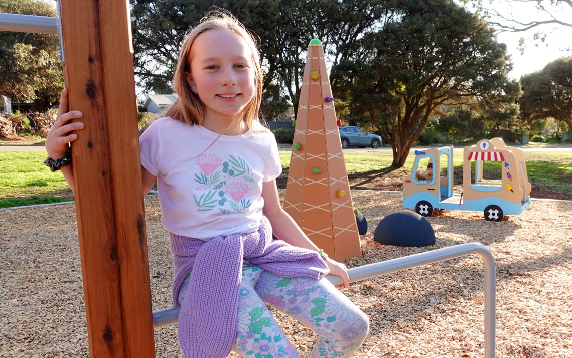 Young Maslin Beach resident Ruby Cooper sits on some exercise bars at the Jasmine Avenue Park with a climbing tower and ice cream truck play equipment in the background.