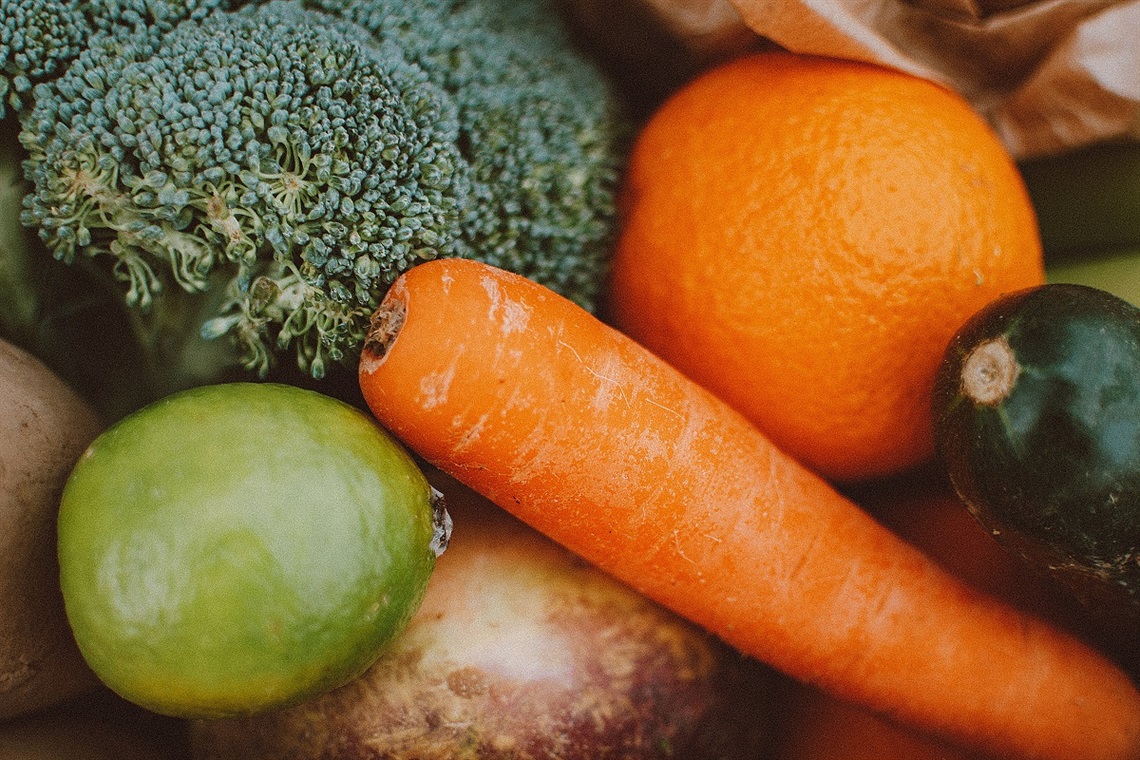 A close-up photo of fruit and vegetables in a pile including broccoli and an orange.