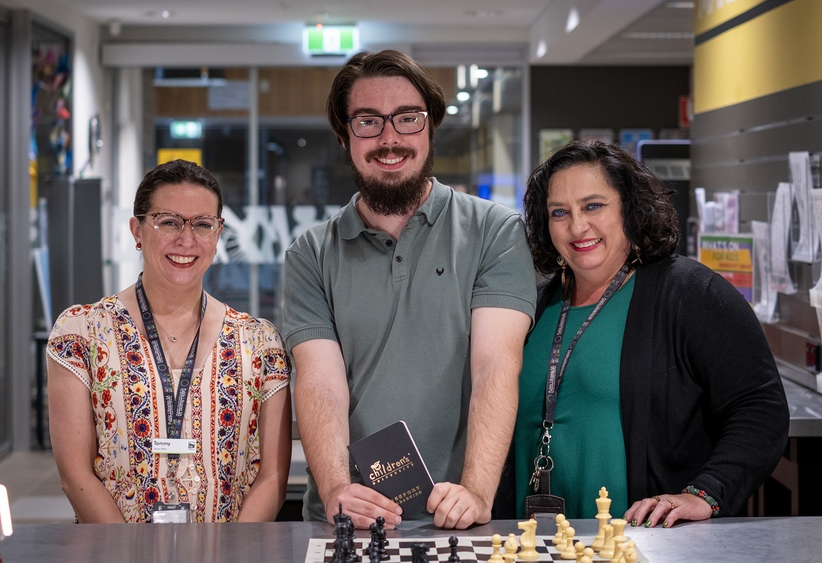 Two smiling City of Onkaparinga staff stand alongside James, a former Children's University participant, who holds his passport.