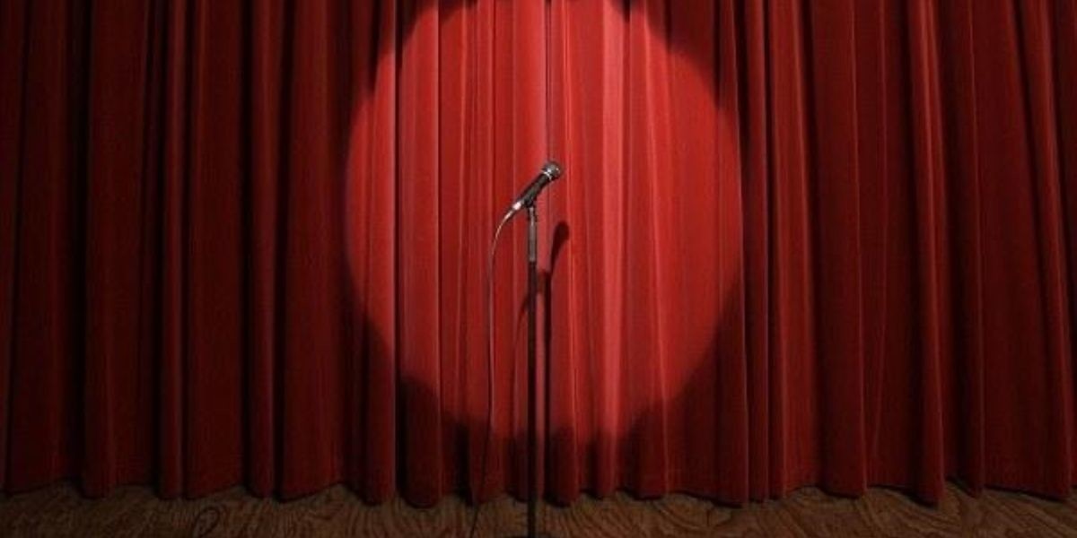 An empty stage with a microphone in front of a red curtain.