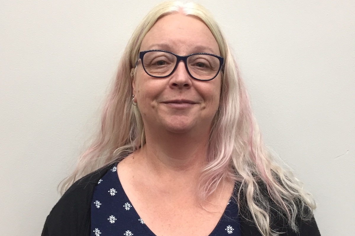 City of Onkaparinga volunteer, Deb, smiles at the camera wearing a pair of glasses, a blue top and a black cardigan.