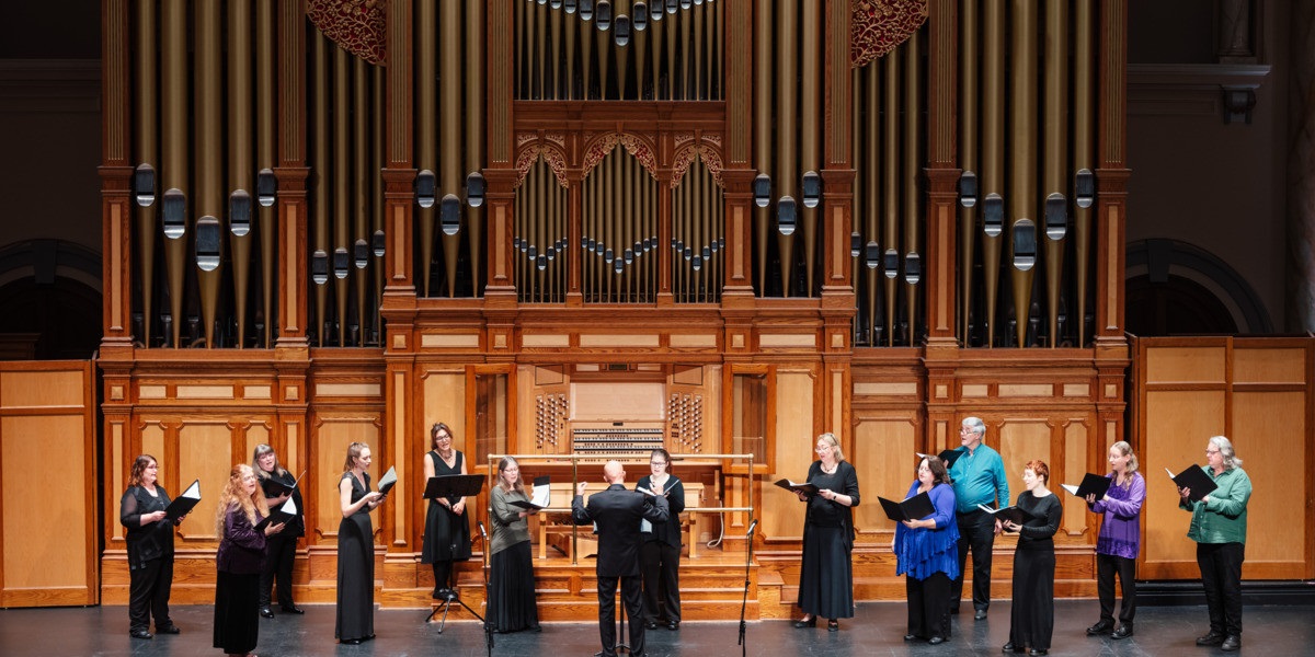 The Lumina Vocal Ensemble perform on stage with a timber organ behind them.