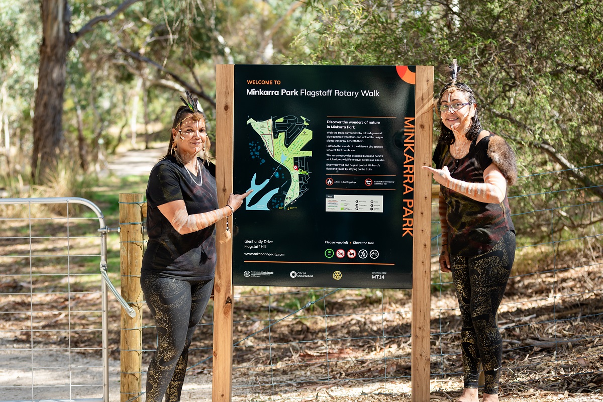 Two smiling women stand alongside the new Minkarra Park Link Path trail signage.