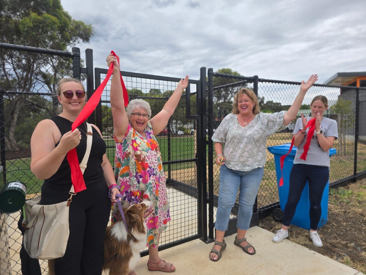 A photo of four women with a cut red ribbon celebrating the opening of the Woodcroft Dog Park.